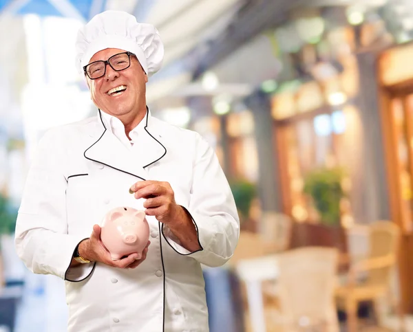 Chef colocando moeda em Piggybank, interior — Fotografia de Stock