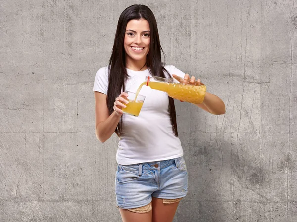 Retrato de uma jovem mulher derramando um suco de laranja em um copo — Fotografia de Stock