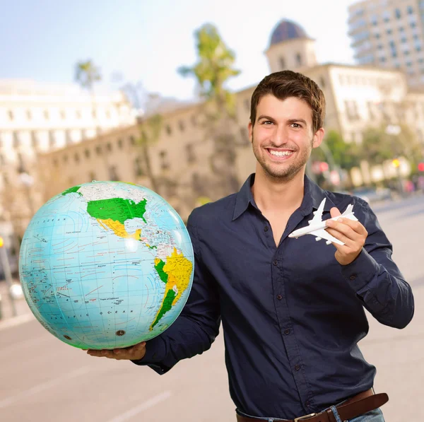 Молодой человек держит глобус и миниатюру — стоковое фото