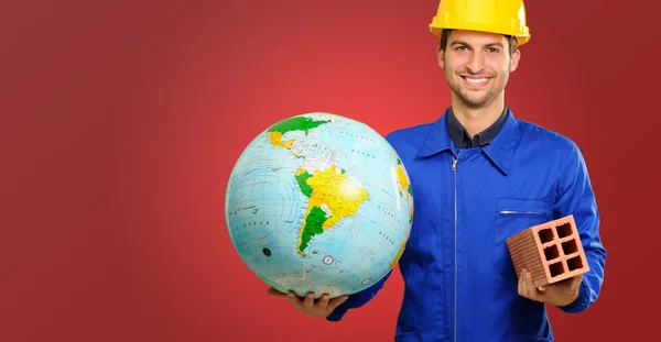Feliz jovem trabalhador de construção segurando globo e tijolo — Fotografia de Stock