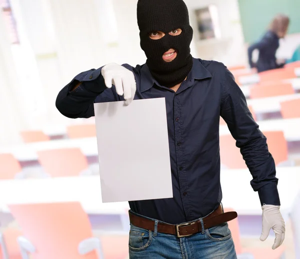 Homem usando uma máscara de ladrão mostrando um papel em branco — Fotografia de Stock