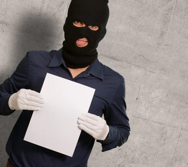 Homem usando uma máscara de ladrão mostrando um papel em branco — Fotografia de Stock