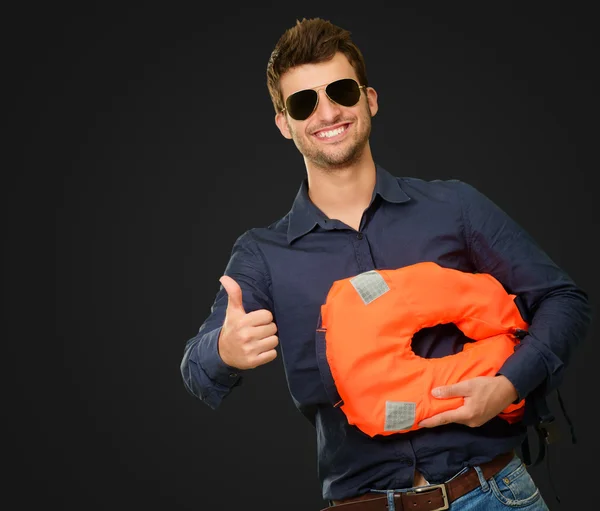 Felice giovane uomo tenendo giubbotto di salvataggio e mostrando pollice fino segno — Foto Stock