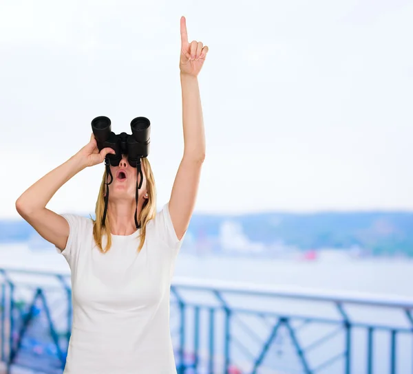 Woman looking through binoculars and pointing up — Stock Photo, Image