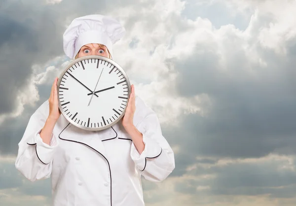 Worried chef hiding behind a clock — Stock Photo, Image