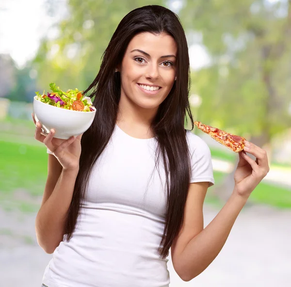 Vrouw houdt een stuk van pizza en salade kom — Stockfoto
