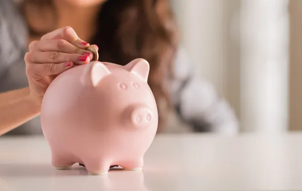 Vrouw zetten munt in Piggy Bank Stockafbeelding