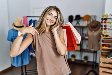 Alışveriş torbalarını tutan genç sarışın kadın kendine güvenen, yüzünde gülümseme olan, kendini gururlu ve mutlu bir şekilde gösteren.. 