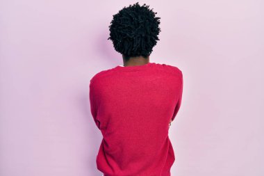 Gündelik giysiler giymiş genç Afro-Amerikan bir adam arkasını dönüp kollarını kavuşturarak başka tarafa bakıyor. 