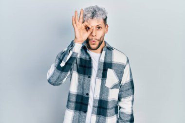 Modern boyalı saçı olan, normal tişörtler giyen, şaşırmış yüz ifadesiyle şaşırmış, parmaklarından bakan genç İspanyol bir adam. İnançsız ifade. 