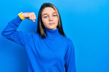 Balıkçı yaka kazak giyen genç esmer kız güçlü kol kası gösteren, kendinden emin ve güçle gurur duyan biri. 