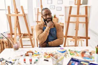 African american artist man at art studio looking confident at the camera with smile with crossed arms and hand raised on chin. thinking positive. 