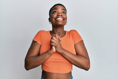 Genç Afro-Amerikalı kadın, günlük turuncu tişört giyiyor. Elleriyle yalvarıyor ve dua ediyor. Yüzünde umut ifadesi var. Yalvarıyor. 