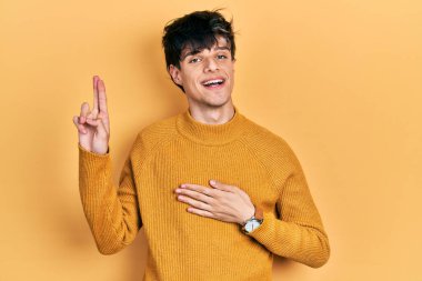 Yakışıklı hippi genç adam gündelik sarı süveter giyiyor. Gülümsüyor, elleri göğsünde ve parmakları havada küfür ediyor. Sadakat yemini ediyor. 