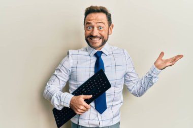 Orta yaşlı iş adamı elinde klavye tutarak başarıyı mutlu bir gülümsemeyle ve kazanan ifadeyle kutluyor. 