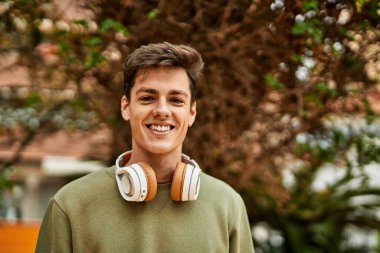 Şehirde kulaklık takarak mutlu gülümseyen genç İspanyol adam..