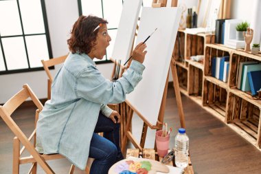 Orta yaşlı İspanyol kadın resim stüdyosunda tuvale resim yapıyor. Korkmuş ve şaşırmış bir şekilde ağzı açık, inançsız bir yüz. 