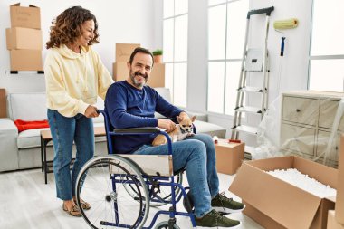 Orta yaşlı İspanyol çift mutlu gülümsüyor. Tekerlekli sandalyede oturan bir adam ve yeni evinde ayakları üzerinde duran bir köpek.