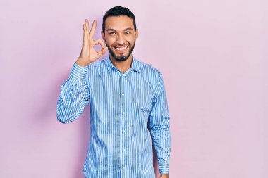 Sakallı, sıradan mavi tişörtlü, gülümseyen İspanyol adam el ve parmaklarıyla 