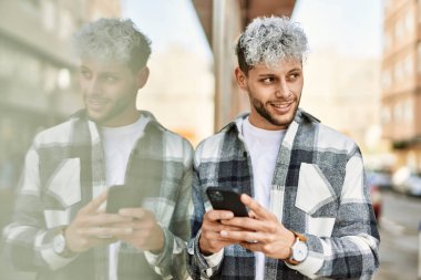 Genç İspanyol adam şehirde akıllı telefon kullanarak mutlu gülümsüyor..