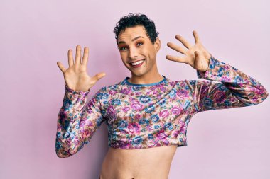 Makyaj giysileri giymiş yakışıklı bir adam dokuz numarayı gösterip işaret ederken kendine güvenen ve mutlu bir şekilde gülümsüyor.. 