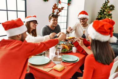 Bir grup genç, mutlu bir şekilde gülümseyerek evde Noel yemeği yiyor..
