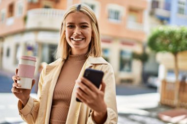 Genç sarışın kız şehirde kahve içerken akıllı telefon kullanıyor..