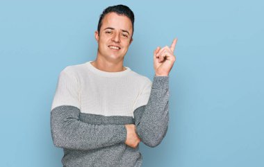 Yakışıklı, sıradan bir kazak giyen, yüzünde kocaman bir gülümseme olan, eli ve parmağı kameraya bakan genç bir adam.. 