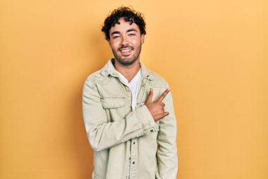 Yüzünde mutlu ve doğal bir ifade olan, elleri ve parmaklarıyla işaret eden, güler yüzlü, gündelik kıyafetler giyen genç İspanyol adam. 