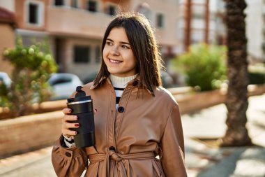 Genç ve güzel esmer kadın mutlu bir şekilde dışarıda gülüyor. Bir fincan kahve içiyor.