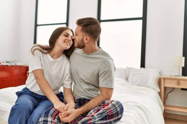 Genç beyaz çift mutlu bir şekilde gülümsüyor ve evdeki yatakta sarılıyorlar.