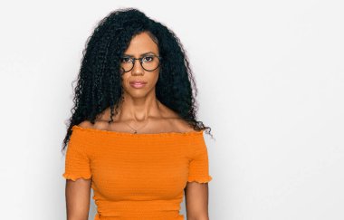Orta yaşlı Afro-Amerikalı kadın günlük kıyafetler ve gözlük takıyor. Yüzünde ciddi bir ifadeyle rahatlıyor. Basit ve doğal bir şekilde kameraya bakıyorsun.. 