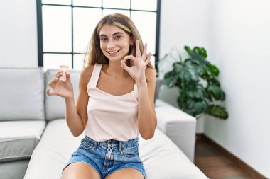 Genç sarışın kadın elinde regl fincanı tutuyor. Parmaklarıyla imza atıyor. Gülümsüyor. 