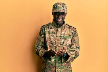 Asker üniforması giymiş, elleri avuçlarında gülümseyen, el hareketi yapan genç Afro-Amerikan bir adam. Bekleme ve koruma 