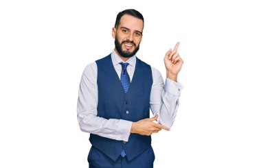 Sakallı, iş yeleği giyen, yüzünde kocaman bir gülümseme olan, eli ve parmağı kameraya bakan genç bir adam.. 