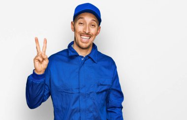 Sakallı, inşaatçı tulumu giyen kel bir adam iki numaralı parmaklarıyla kendini gösterip gülümsüyor ve mutlu.. 