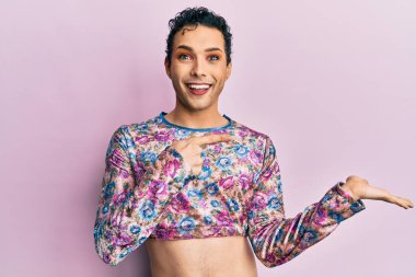 Makyaj giysileri giyen yakışıklı bir adam hayret içinde kameraya gülümserken eliyle ve parmağıyla işaret ediyor.. 