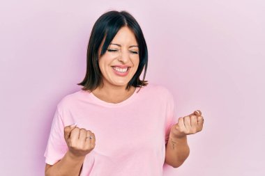 Kolları havada ve gözleri kapalı zaferi kutlayan günlük pembe tişört giyen genç İspanyol kadın. Kazanan konsept. 