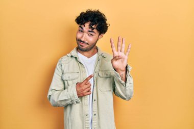 İspanyol asıllı genç adam, gündelik giysiler giyip dört numarayı gösterip işaret ederken kendinden emin ve mutlu bir şekilde gülümsüyor.. 