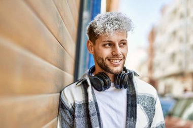 Şehirde kulaklık takarak mutlu gülümseyen genç İspanyol adam..