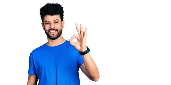ひげを生やした若いアラブ人男性は 手と指でOkサインをして肯定的な笑みを浮かべてカジュアルな青のTシャツを着ています 成功した表現 — ストック写真