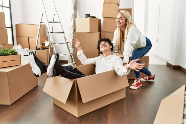 Young beautiful couple smiling happy playing using cardboard box as a car at new home.