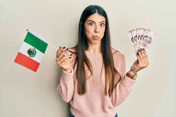 メキシコの国旗とメキシコペソの紙幣を持っている若いヒスパニック系の女性は 面白い顔で頬をむいています 空気を吸い込み空気を吸い込み — ストック写真