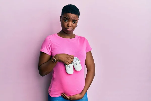 Mujer Afroamericana Joven Esperando Bebé Sosteniendo Zapatos Escéptico Nervioso Frunciendo — Foto de Stock