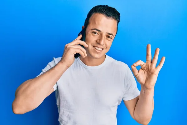 スマートフォンで会話をしているハンサムな若い男が指でOkサインをして 優しいジェスチャー素晴らしいシンボル — ストック写真