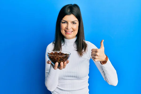 Mujer Hispana Joven Sosteniendo Tazón Pasas Sonriendo Feliz Positivo Pulgar — Foto de Stock