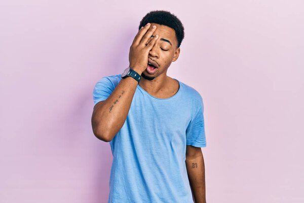 Young african american man wearing casual blue t shirt yawning tired covering half face, eye and mouth with hand. face hurts in pain. 