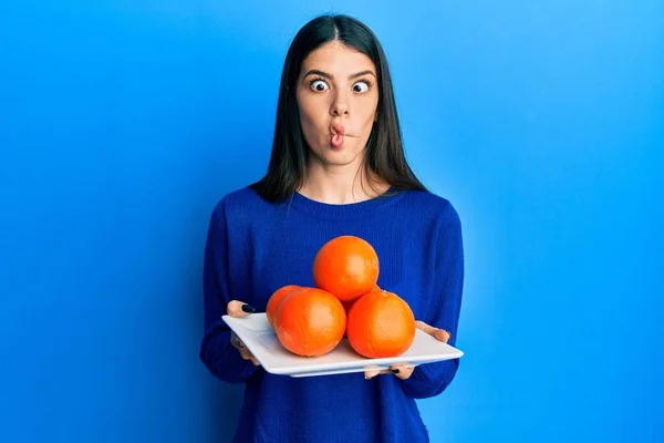 年轻的惊慌失措的女人拿着用新鲜的橙子做的盘子 用嘴和眼神做鱼的脸 疯狂而滑稽 — 图库照片