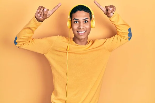 一个年轻的非洲裔美国人 一边用耳机听着音乐 一边笑着 惊讶着 用手指和胳膊指指着音乐 — 图库照片