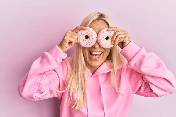 Ung Blond Kvinna Håller Välsmakande Rosa Munkar Över Ögonen Ler — Stockfoto